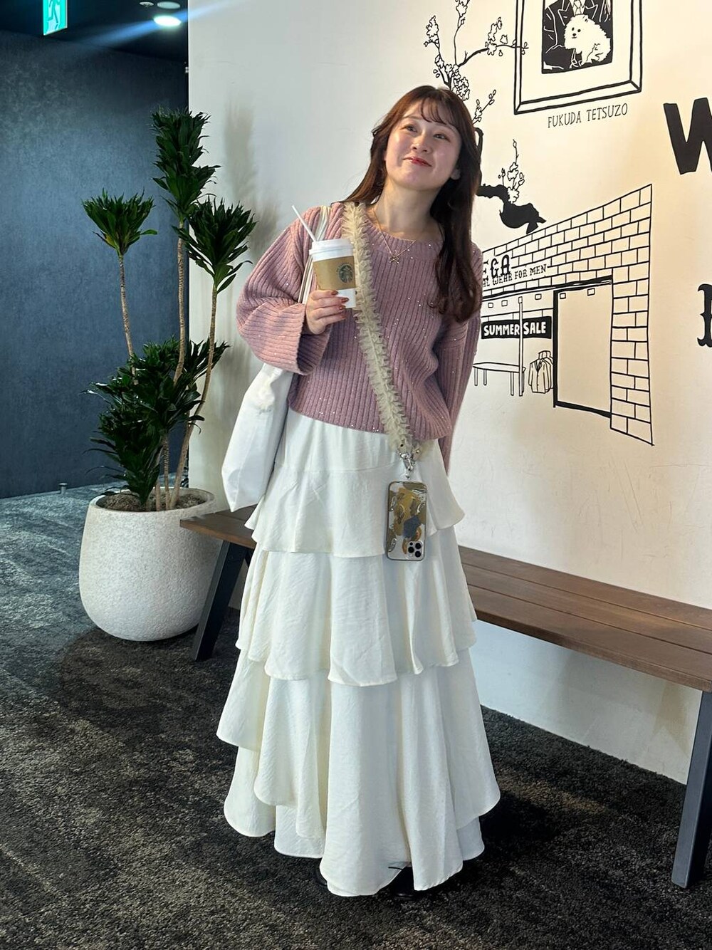 ホワイト系のスカート、ピンク系のニット/セーター、ベージュ系のスマホグッズを着用したレディースの秋コーディネートの1枚目の写真