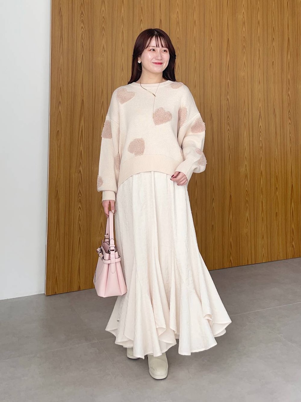 ピンク系のショルダーバッグ、ホワイト系のブーツ、ホワイト系のスカートを着用したレディースの冬コーディネートの1枚目の写真