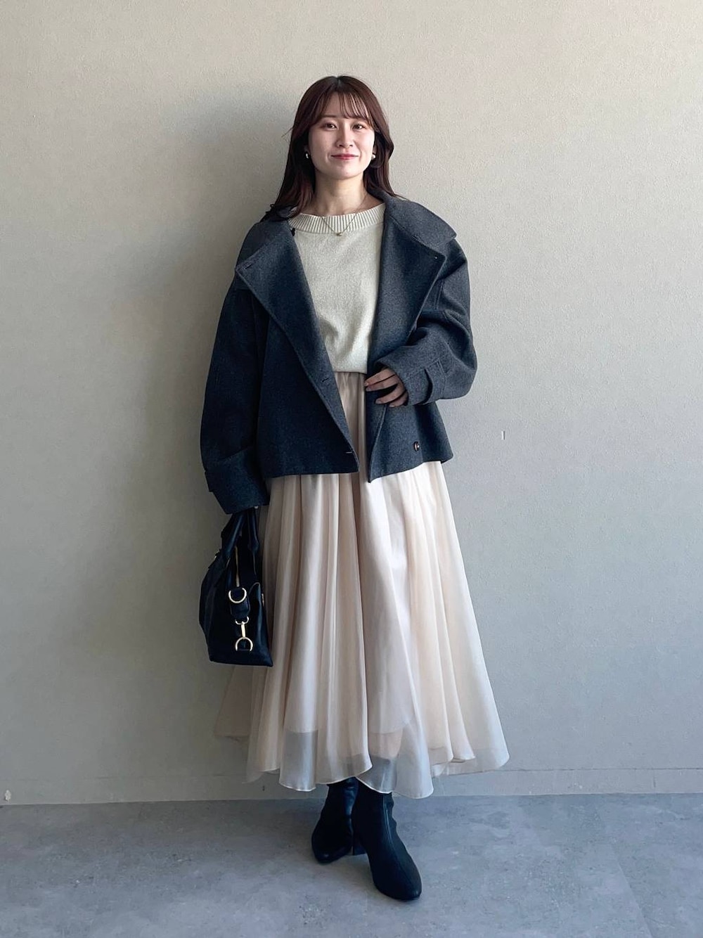 グレー系のピーコート、ホワイト系のニット/セーター、ブラック系のボストンバッグを着用したレディースの冬コーディネートの1枚目の写真
