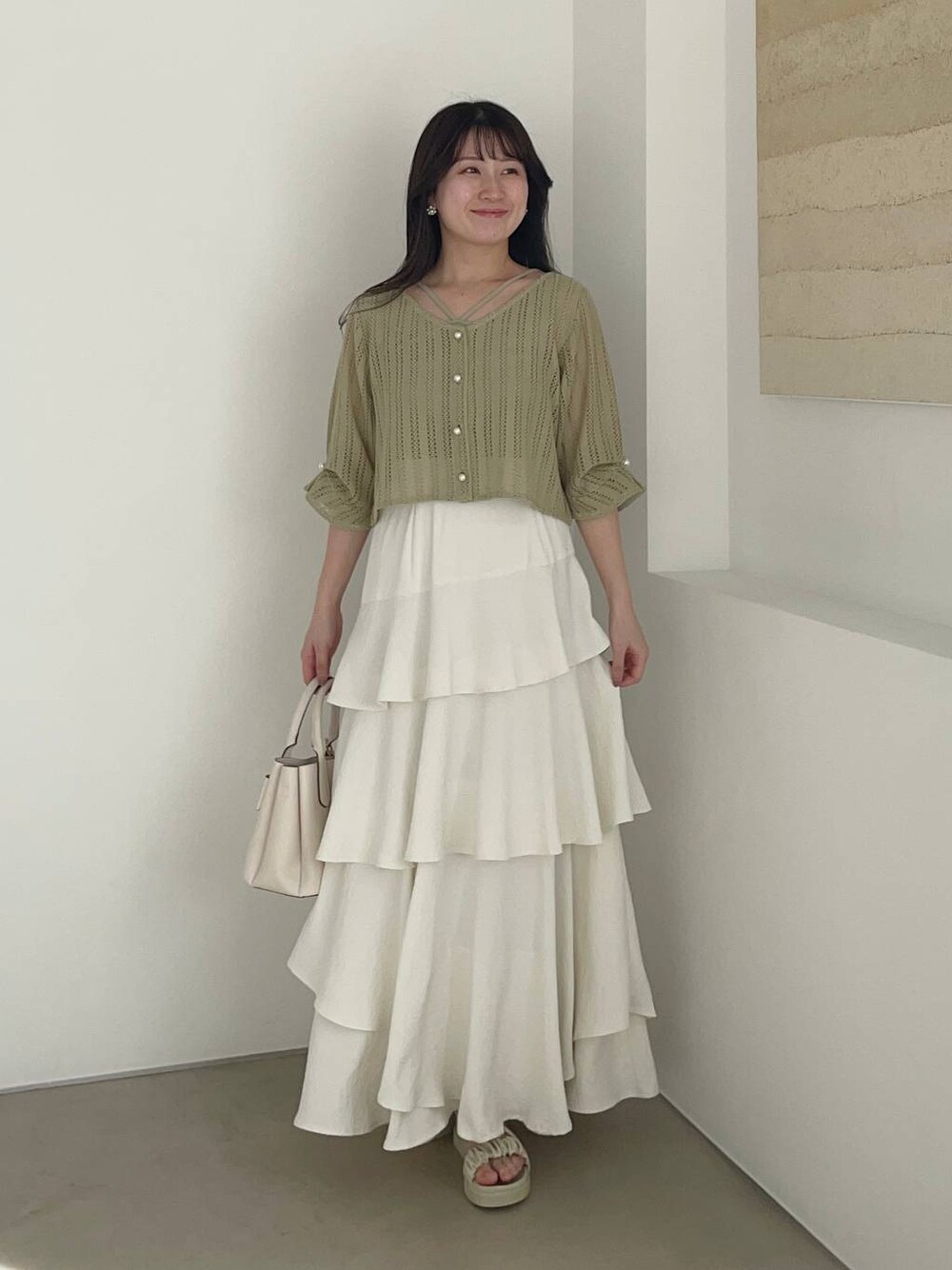 ホワイト系のスカート、ホワイト系のショルダーバッグ、グリーン系のカーディガン/ボレロを着用したレディースの春コーディネートの1枚目の写真