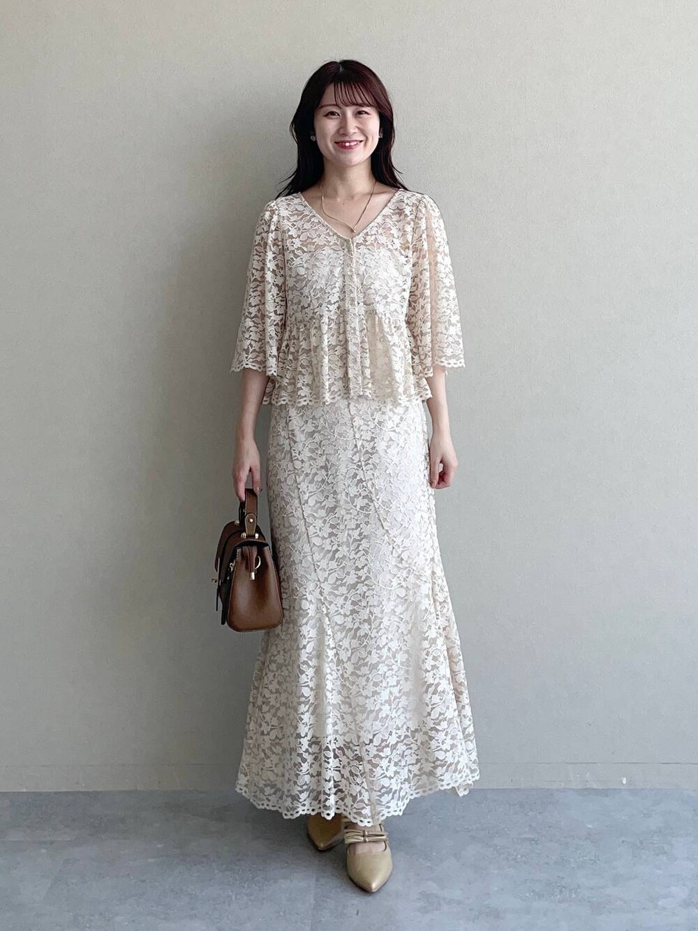 ゴールド系のパンプス、ブラウン系のショルダーバッグ、ベージュ系のシャツ/ブラウスを着用したレディースの夏コーディネートの1枚目の写真