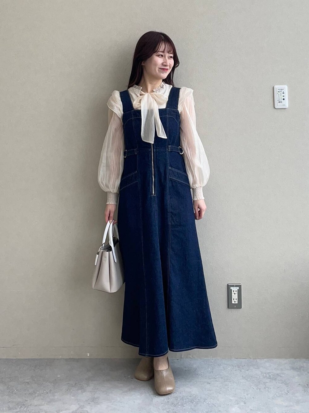 ブルー系のジャンパースカート、ベージュ系のショルダーバッグ、ブラウン系のパンプスを着用したレディースの冬コーディネートの1枚目の写真