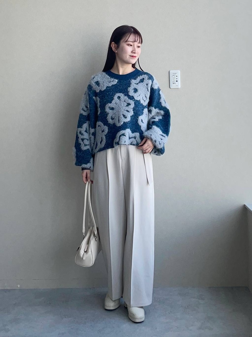 ブルー系のニット/セーター、ホワイト系のブーツ、ホワイト系のハンドバッグを着用したレディースの冬コーディネートの1枚目の写真