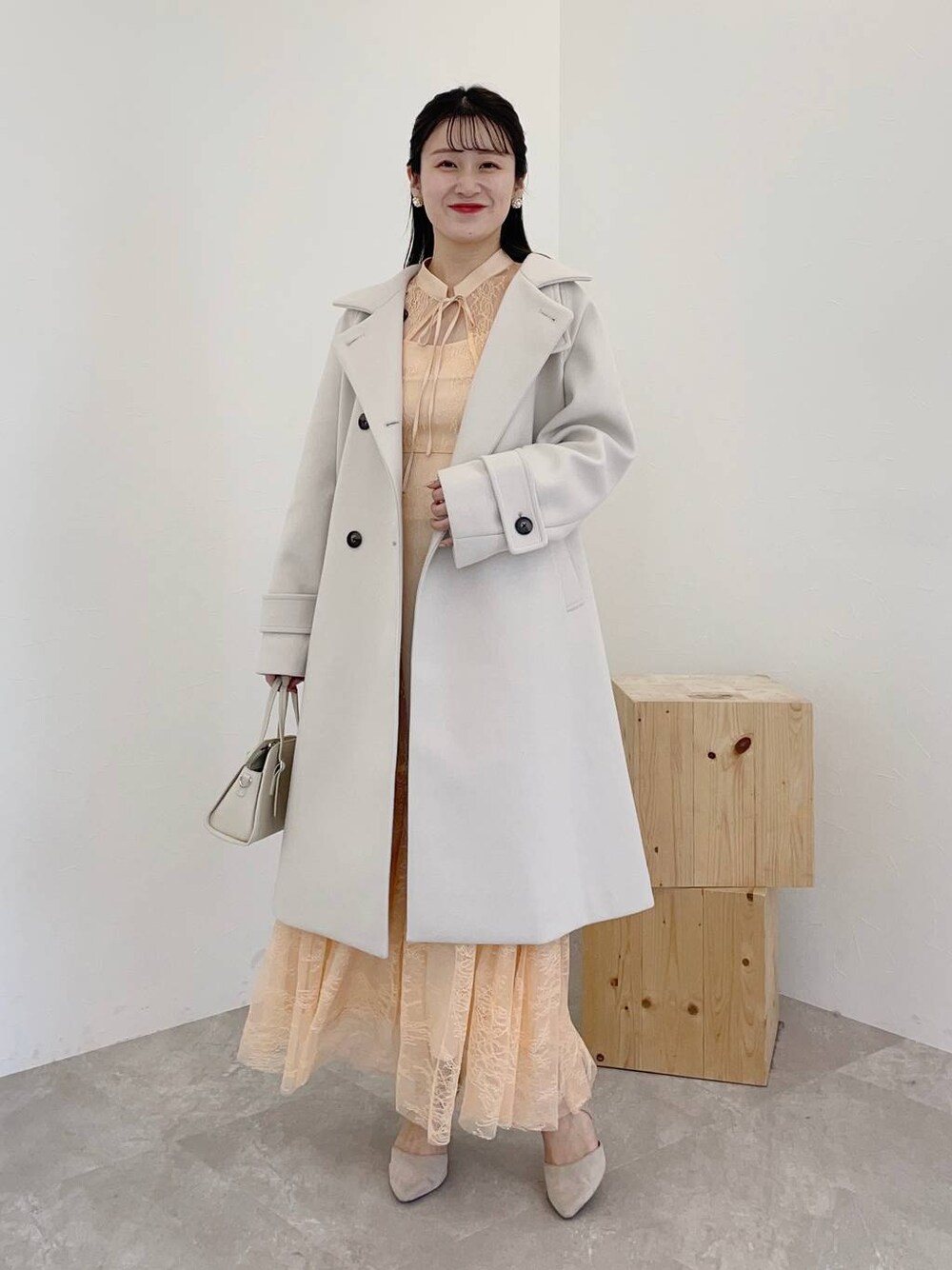 グレー系のパンプス、ホワイト系のボストンバッグ、ホワイト系のチェスターコートを着用したレディースの秋コーディネートの1枚目の写真
