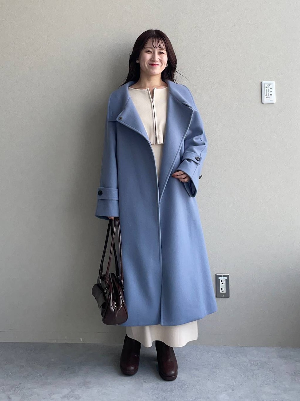 ブルー系のチェスターコート、ブラウン系のブーツ、ホワイト系のワンピースを着用したレディースの冬コーディネートの1枚目の写真