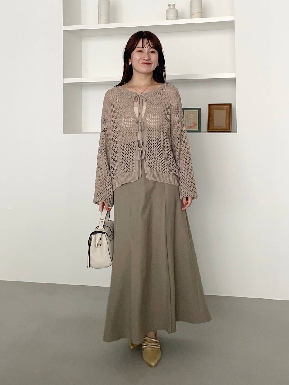 ゴールド系のパンプス、ホワイト系のショルダーバッグ、ベージュ系のニット/セーターを着用したレディースの夏コーディネートの1枚目の写真