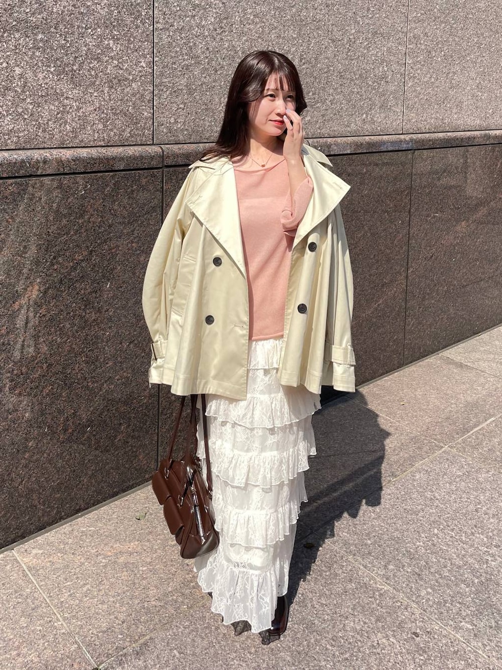 ピンク系のニット/セーター、ブラウン系のハンドバッグ、ベージュ系のトレンチコートを着用したレディースの春コーディネートの1枚目の写真