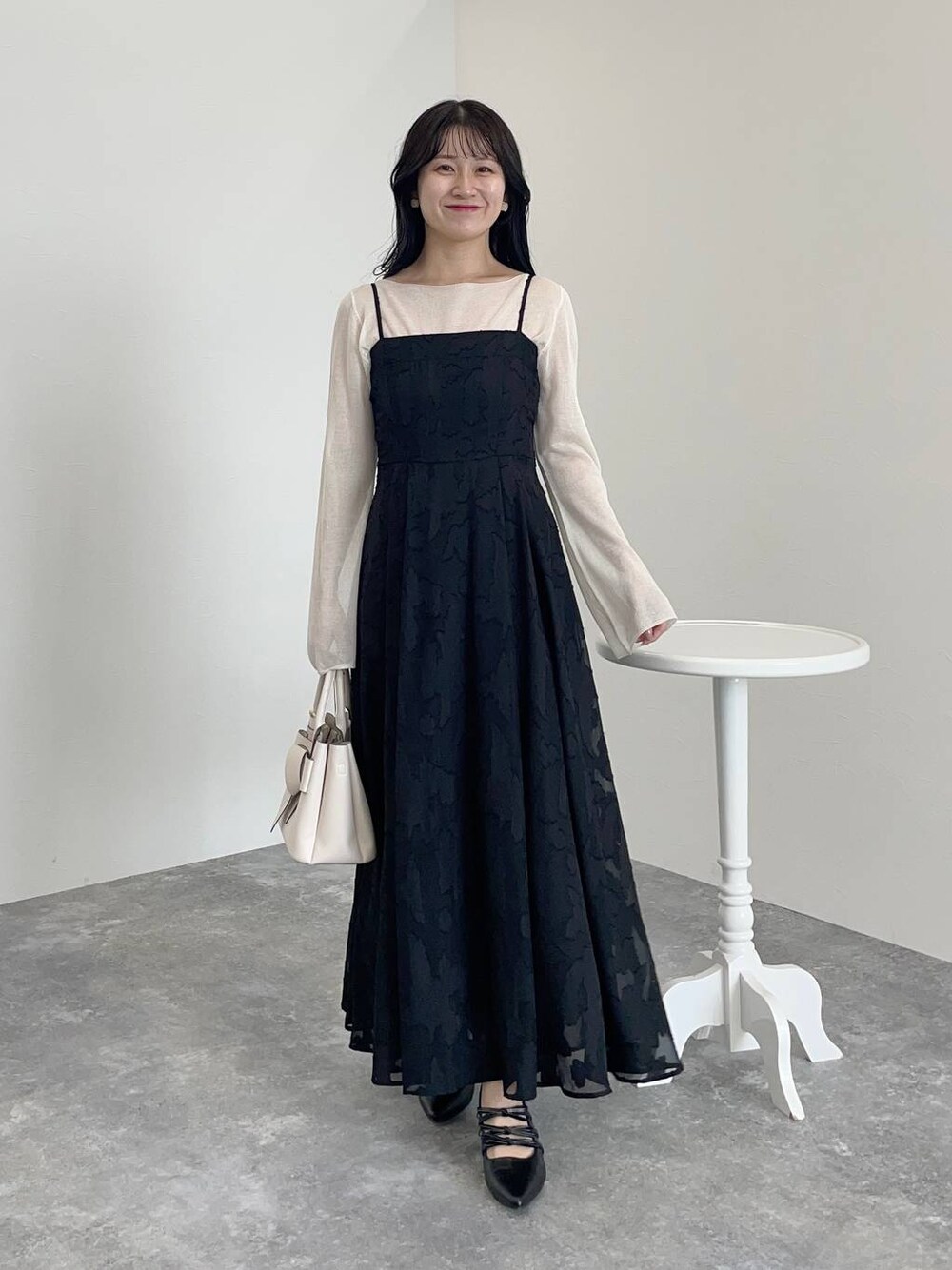 ホワイト系のショルダーバッグ、ブラック系のワンピース、ブラック系のパンプスを着用したレディースの秋コーディネートの1枚目の写真