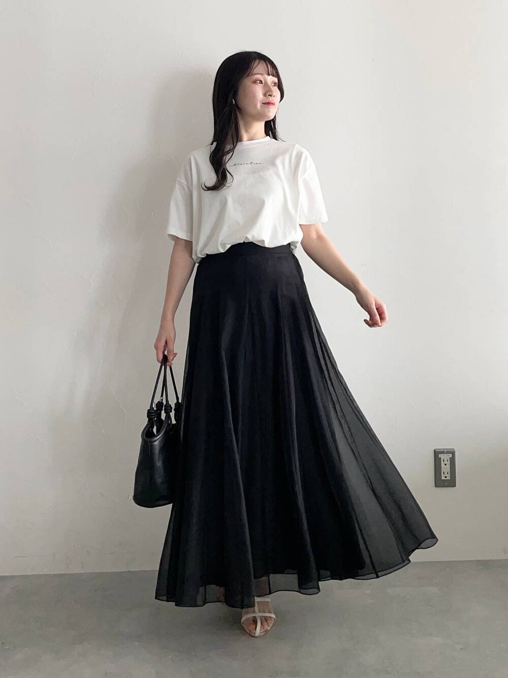 ブラック系のハンドバッグ、ホワイト系のサンダル、ブラック系のスカートを着用したレディースの春コーディネートの1枚目の写真