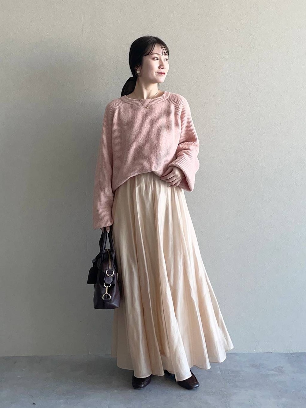 ピンク系のニット/セーター、ブラウン系のボストンバッグ、ベージュ系のスカートを着用したレディースの冬コーディネートの1枚目の写真
