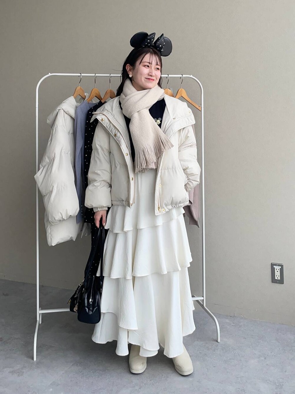 ホワイト系のブーツ、ホワイト系のスカート、ブラック系のハンドバッグを着用したレディースの秋コーディネートの1枚目の写真