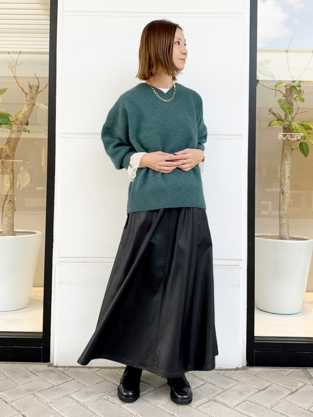 グリーン系のニット/セーター、ブラック系のジャンパースカートを着用したレディースの秋コーディネートの1枚目の写真