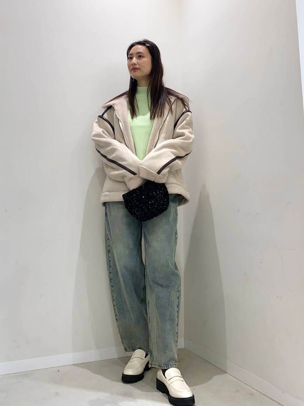 ブラック系のショルダーバッグ、ブルー系のデニムパンツ、ホワイト系のローファーを着用したレディースの冬コーディネートの1枚目の写真