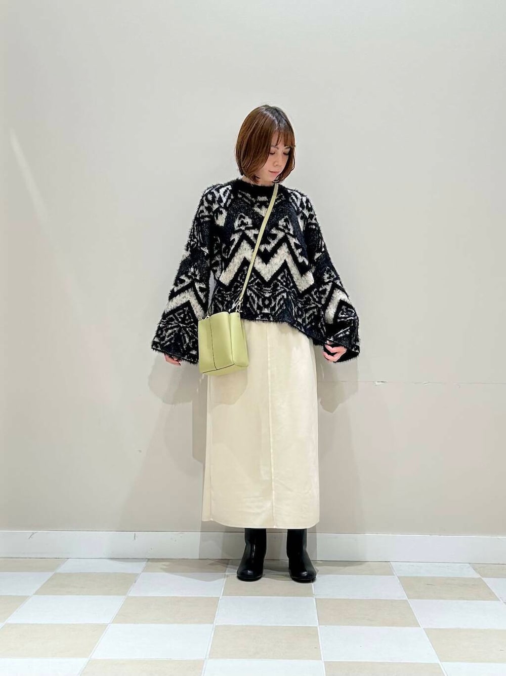 ブラック系のブーツ、グリーン系のショルダーバッグ、ホワイト系のスカートを着用したレディースの冬コーディネートの1枚目の写真