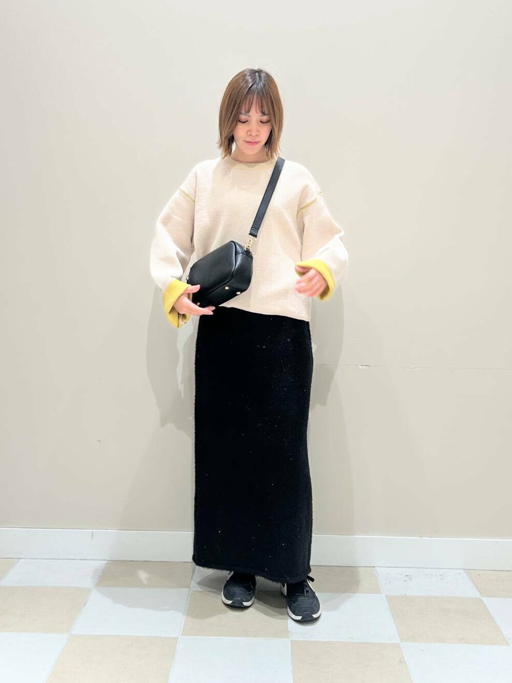 ブラック系のショルダーバッグ、ブラック系のスカート、ホワイト系のニット/セーターを着用したレディースの冬コーディネートの1枚目の写真