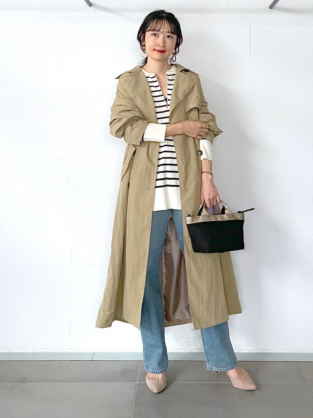 ベージュ系のトレンチコート、ホワイト系のニット/セーター、ブルー系のデニムパンツを着用したレディースの秋コーディネートの1枚目の写真