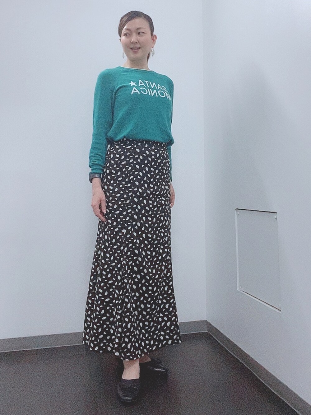 グリーン系のニット/セーター、ブラック系のスカート、ブラック系のレインシューズを着用したレディースの春コーディネートの1枚目の写真