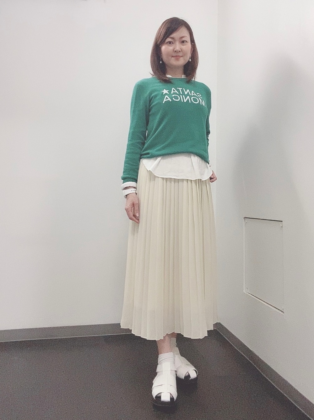 グリーン系のニット/セーター、ホワイト系のスカート、ホワイト系のサンダルを着用したレディースの春コーディネートの1枚目の写真
