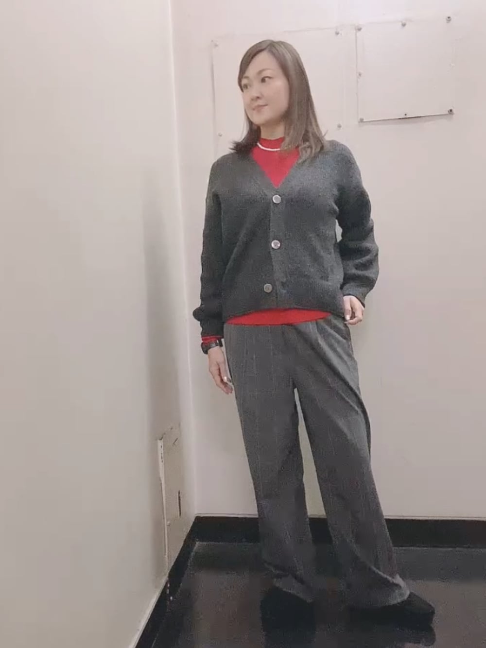 レッド系のニット/セーター、グレー系のスラックス、ブラック系のモカシン/デッキシューズを着用したレディースの冬コーディネートの1枚目の写真
