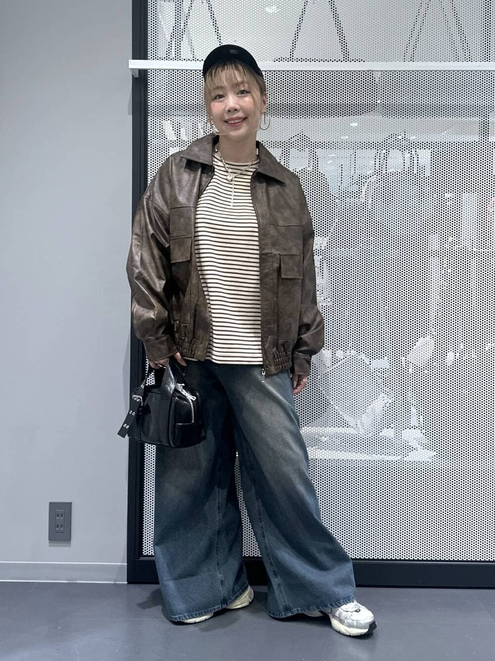 ブラウン系のブルゾン、ブラック系のショルダーバッグ、ブルー系のデニムパンツを着用したレディースの秋コーディネートの1枚目の写真