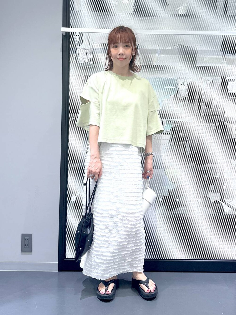 ブラック系のショルダーバッグ、ホワイト系のスカート、グリーン系のTシャツ/カットソーを着用したレディースの夏コーディネートの1枚目の写真