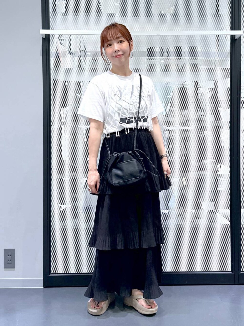 ブラック系のショルダーバッグ、ブラック系のスカート、ベージュ系のサンダルを着用したレディースの夏コーディネートの1枚目の写真