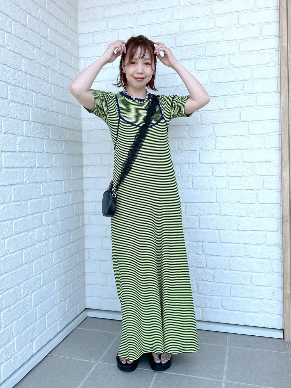 グリーン系のワンピース、ブラック系のサンダル、ブラック系のポーチを着用したレディースの春コーディネートの1枚目の写真