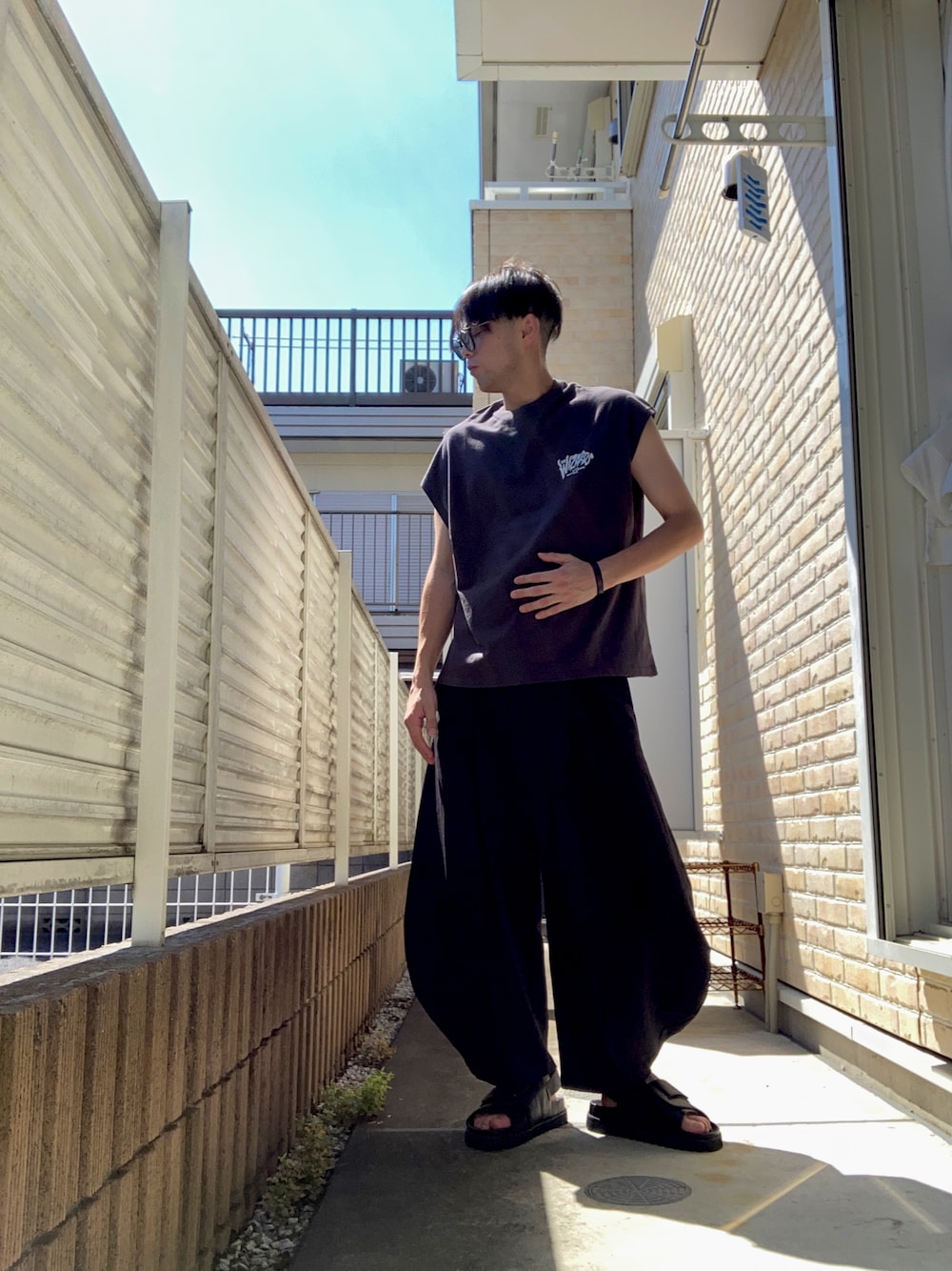 ブラック系のTシャツ/カットソー、ブラック系のスラックス、ブラック系のサンダルを着用したメンズの夏コーディネートの1枚目の写真