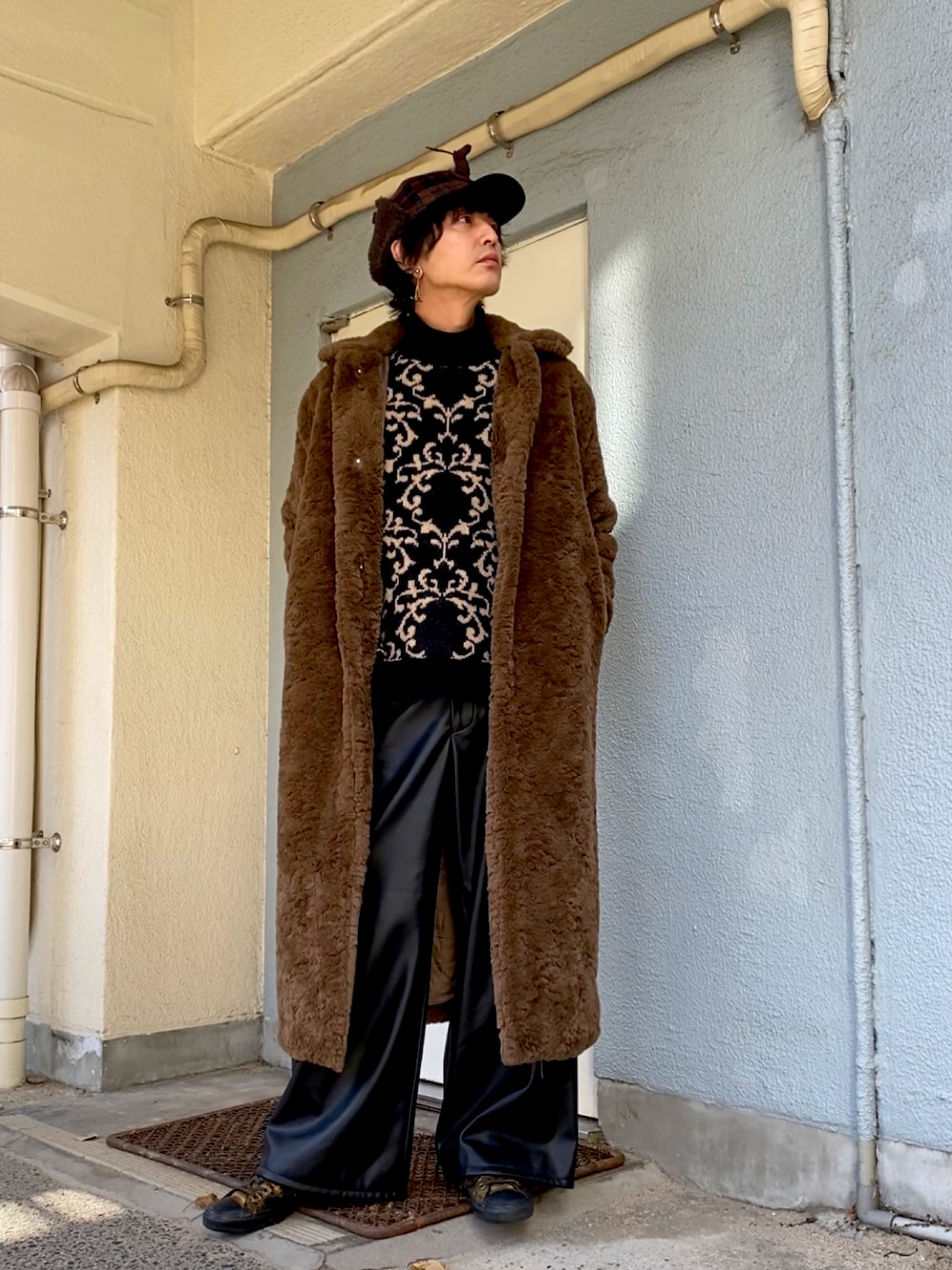 ブラック系のニット/セーター、ブラウン系のチェスターコート、ブラック系のその他パンツを着用したメンズの冬コーディネートの1枚目の写真