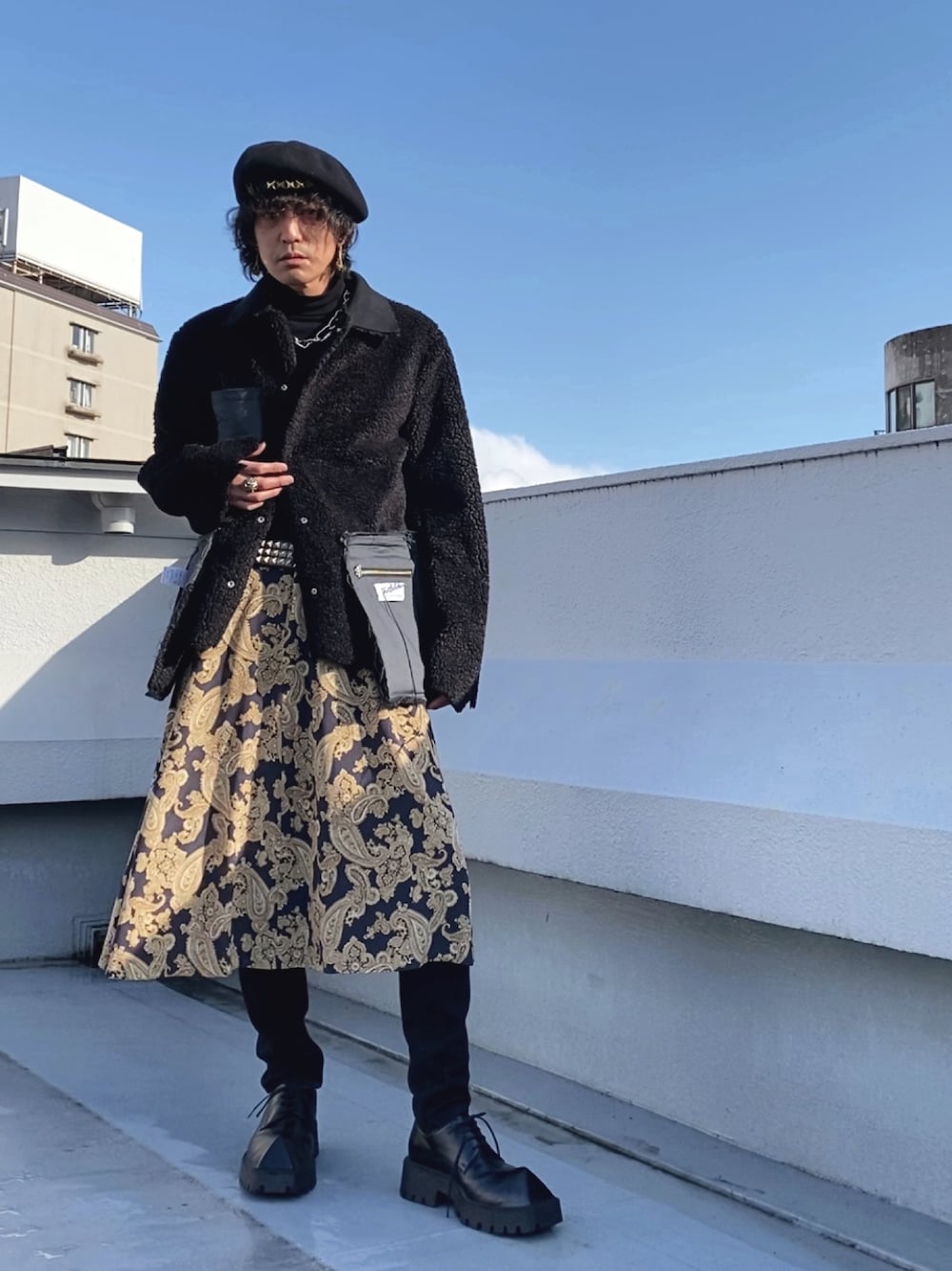 ブラック系のムートンコート、ブルー系のスカート、ブラック系のドレスシューズを着用したメンズの春コーディネートの1枚目の写真