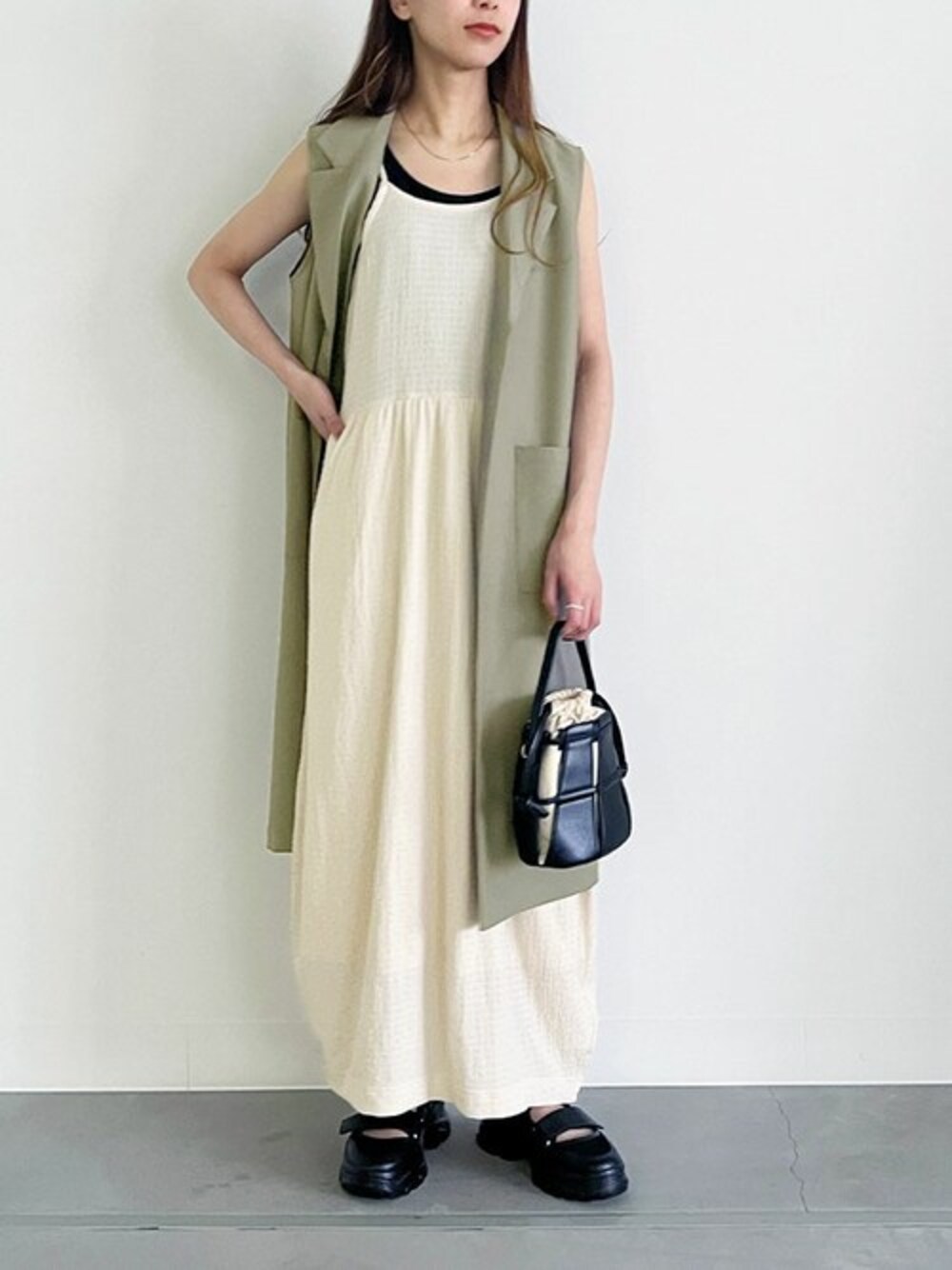 ベージュ系のワンピース、グリーン系のベストを着用したレディースの春コーディネートの1枚目の写真