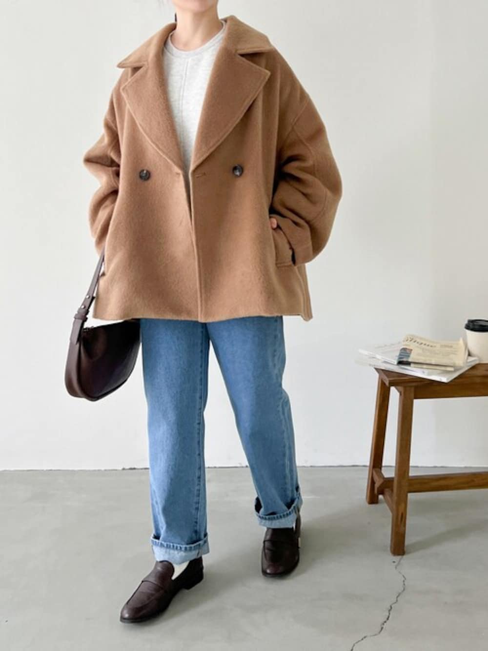 ベージュ系のピーコート、ブルー系のデニムパンツ、ベージュ系のスウェットを着用したレディースの冬コーディネートの1枚目の写真