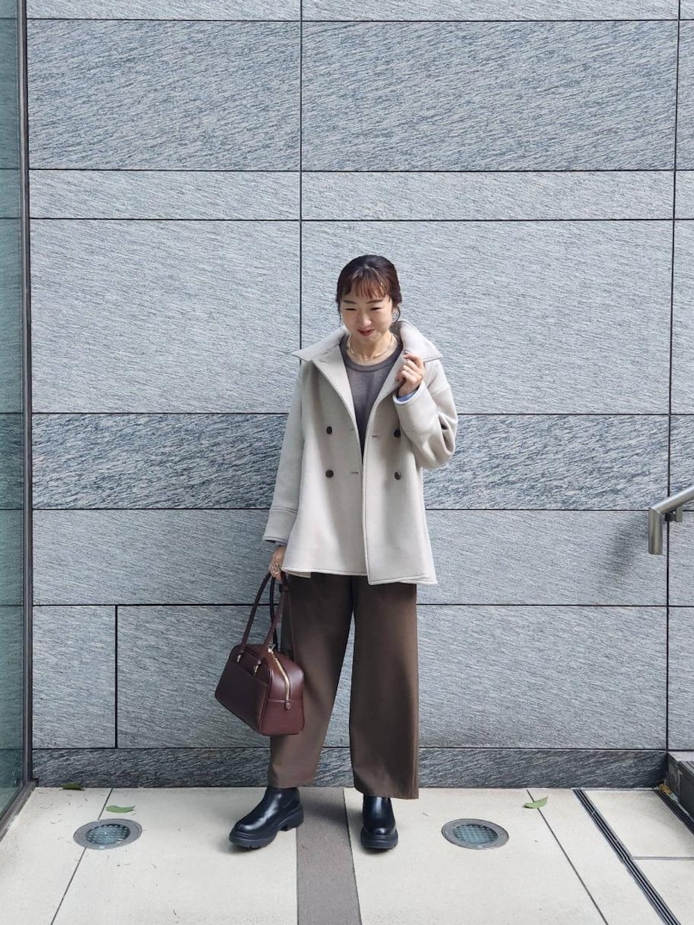 ブラウン系のボストンバッグ、ブラウン系のニット/セーター、ベージュ系のその他アウターを着用したレディースの冬コーディネートの1枚目の写真