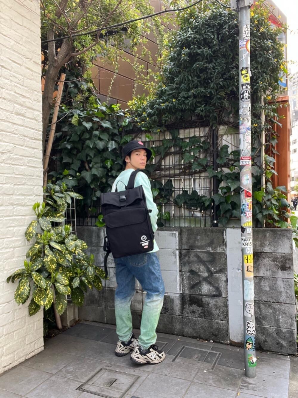 ブラック系のバックパック/リュック、グリーン系のTシャツ/カットソーを着用したメンズの春コーディネートの1枚目の写真