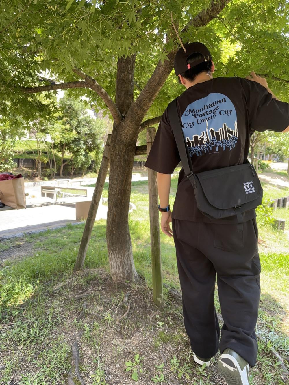 ブラック系のメッセンジャーバッグ、ブラック系のTシャツ/カットソー、ブラック系のキャップを着用したメンズの夏コーディネートの1枚目の写真
