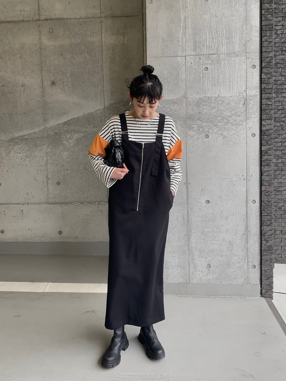 ブラック系のブーツ、オレンジ系のTシャツ/カットソー、ブラック系のジャンパースカートを着用したレディースの春コーディネートの1枚目の写真