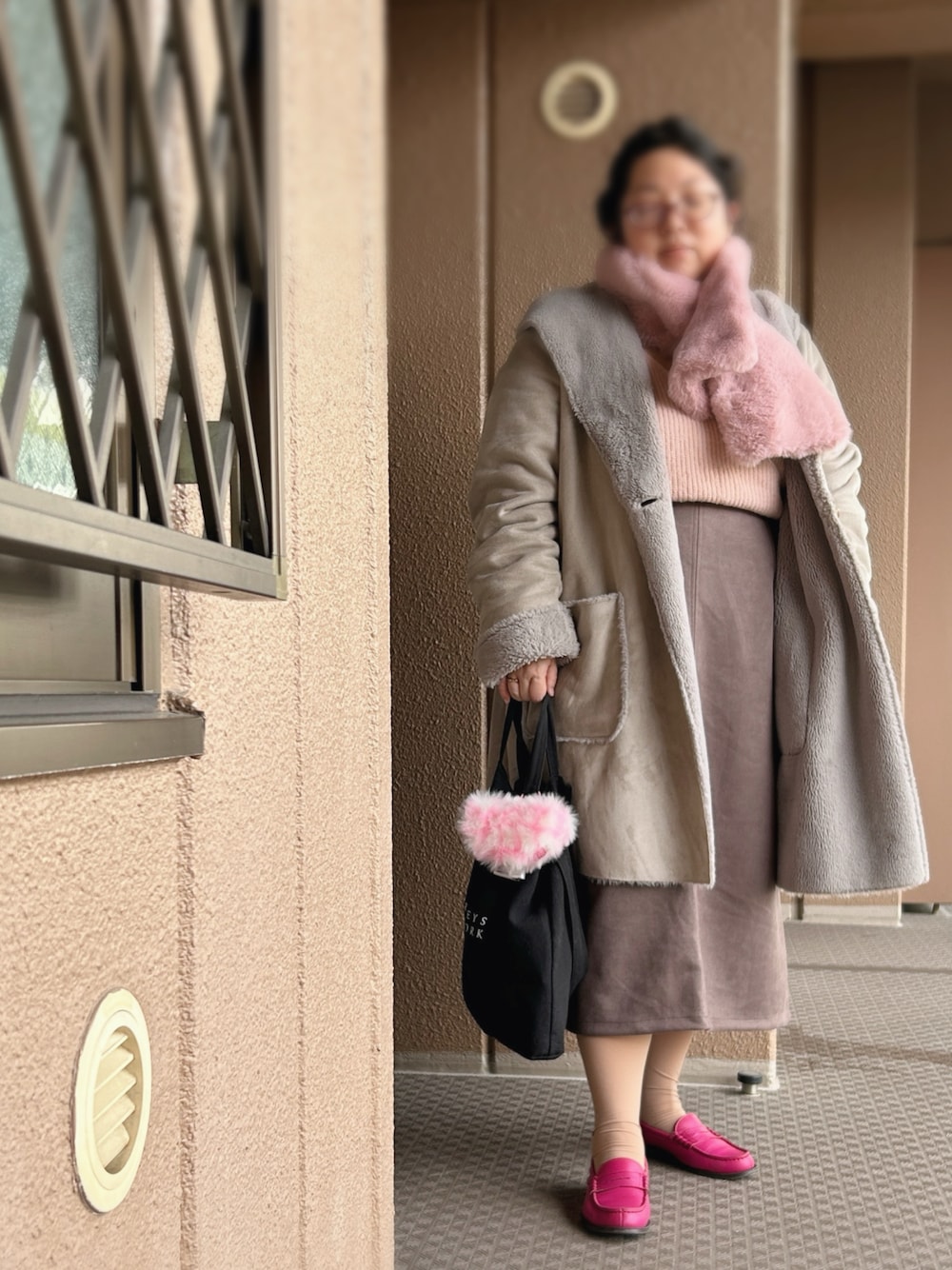 ピンク系のニット/セーター、ブラウン系のスカート、グレー系のムートンコートを着用したレディースの冬コーディネートの1枚目の写真