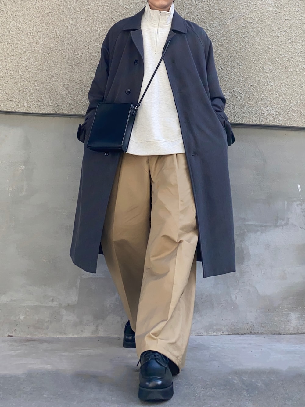グレー系のステンカラーコート、ベージュ系のスウェット、ブラック系のショルダーバッグを着用したメンズの冬コーディネートの1枚目の写真