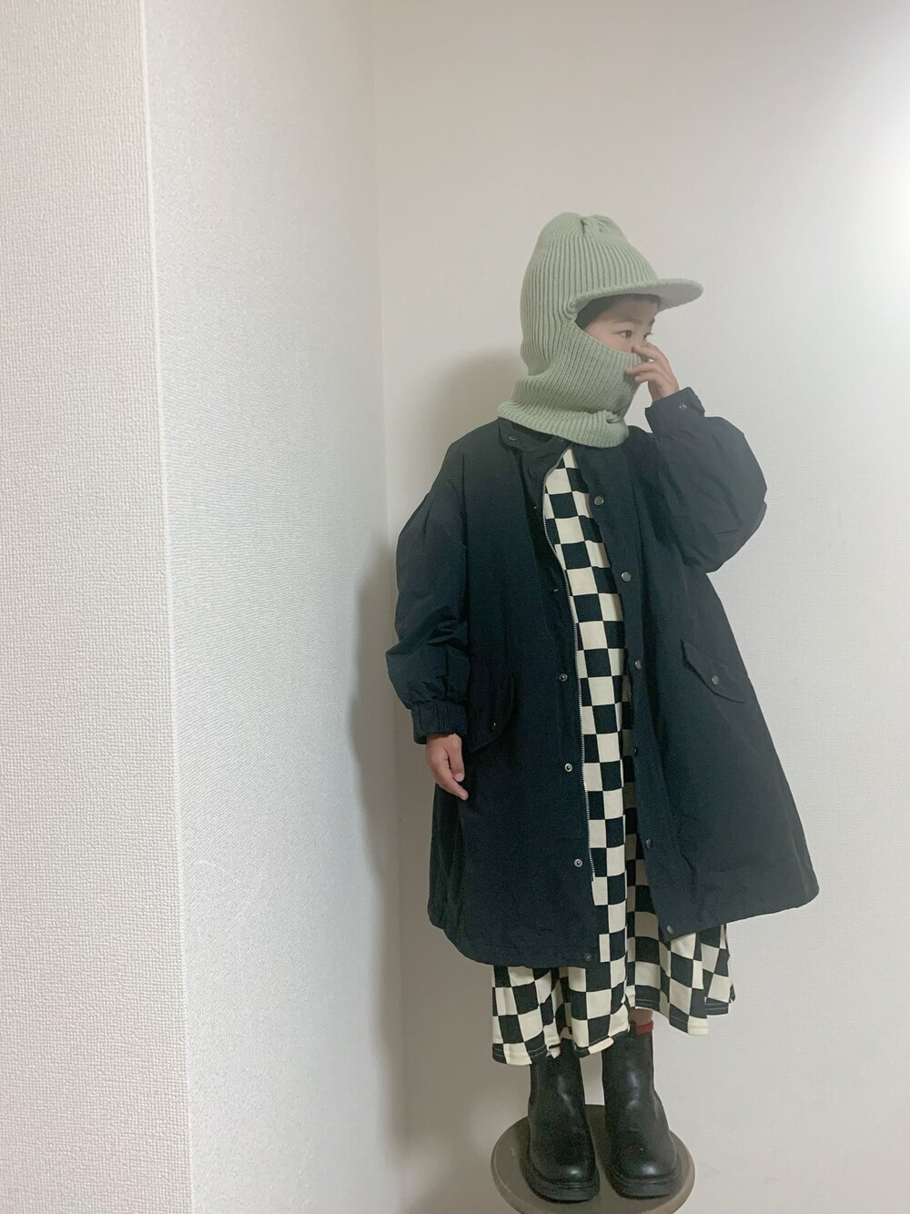 ブラック系のワンピース、ブラック系のモッズコート、グリーン系の帽子を着用したキッズの冬コーディネートの1枚目の写真