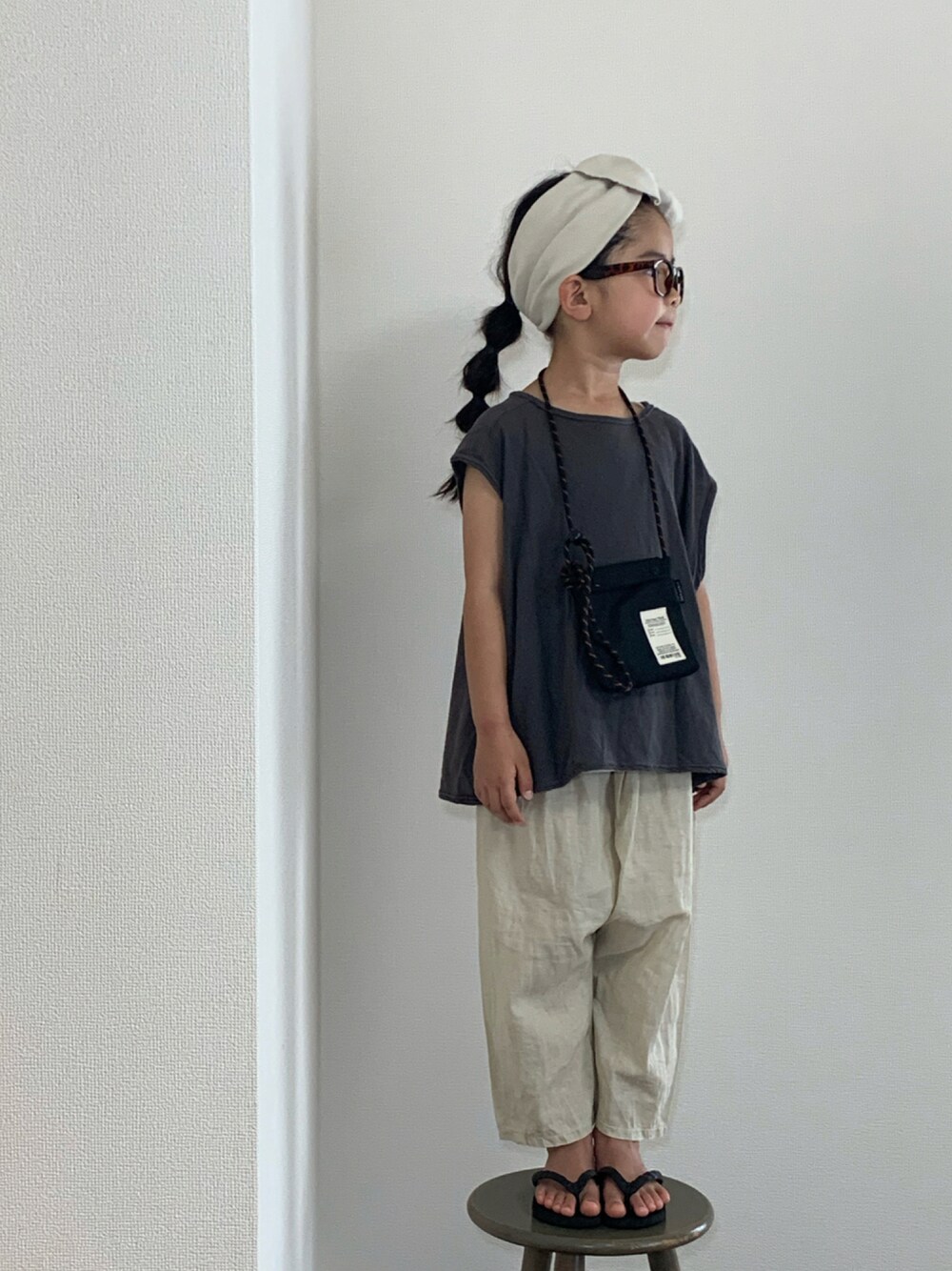 ブラック系のショルダーバッグ、ブラック系のビーチサンダル、ホワイト系のヘアバンドを着用したキッズの夏コーディネートの1枚目の写真