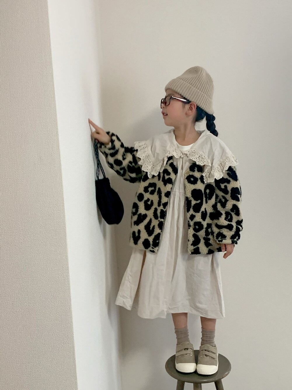 ブラック系のノーカラージャケット、ホワイト系のワンピース、ベージュ系のスニーカーを着用したキッズの秋コーディネートの1枚目の写真
