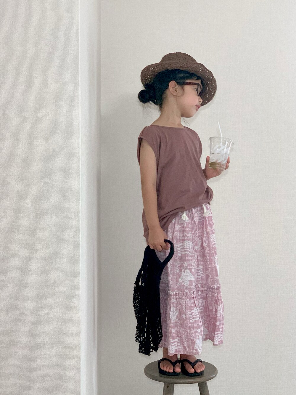 ピンク系のスカート、ブラック系のビーチサンダル、ブラウン系のハットを着用したキッズの夏コーディネートの1枚目の写真