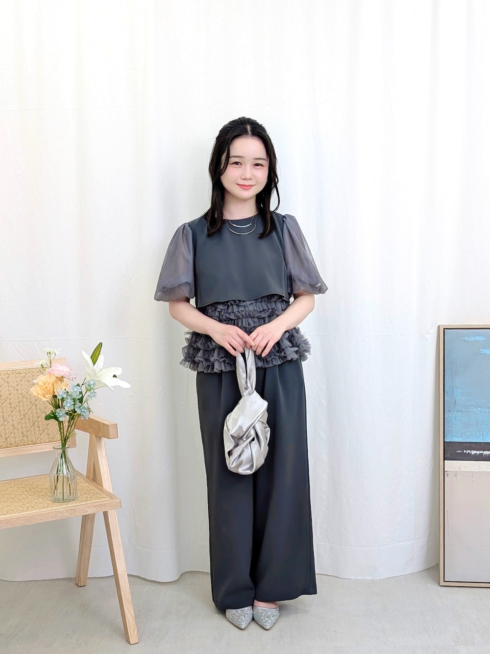 グレー系のパンツドレス、シルバー系のハンドバッグ、シルバー系のパンプスを着用したレディースの春コーディネートの1枚目の写真