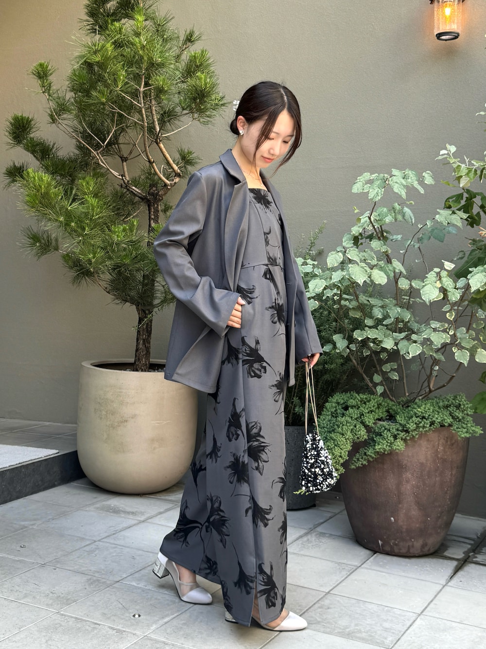シルバー系のパンプス、グレー系のパンツドレス、ブラック系のハンドバッグを着用したレディースの夏コーディネートの1枚目の写真