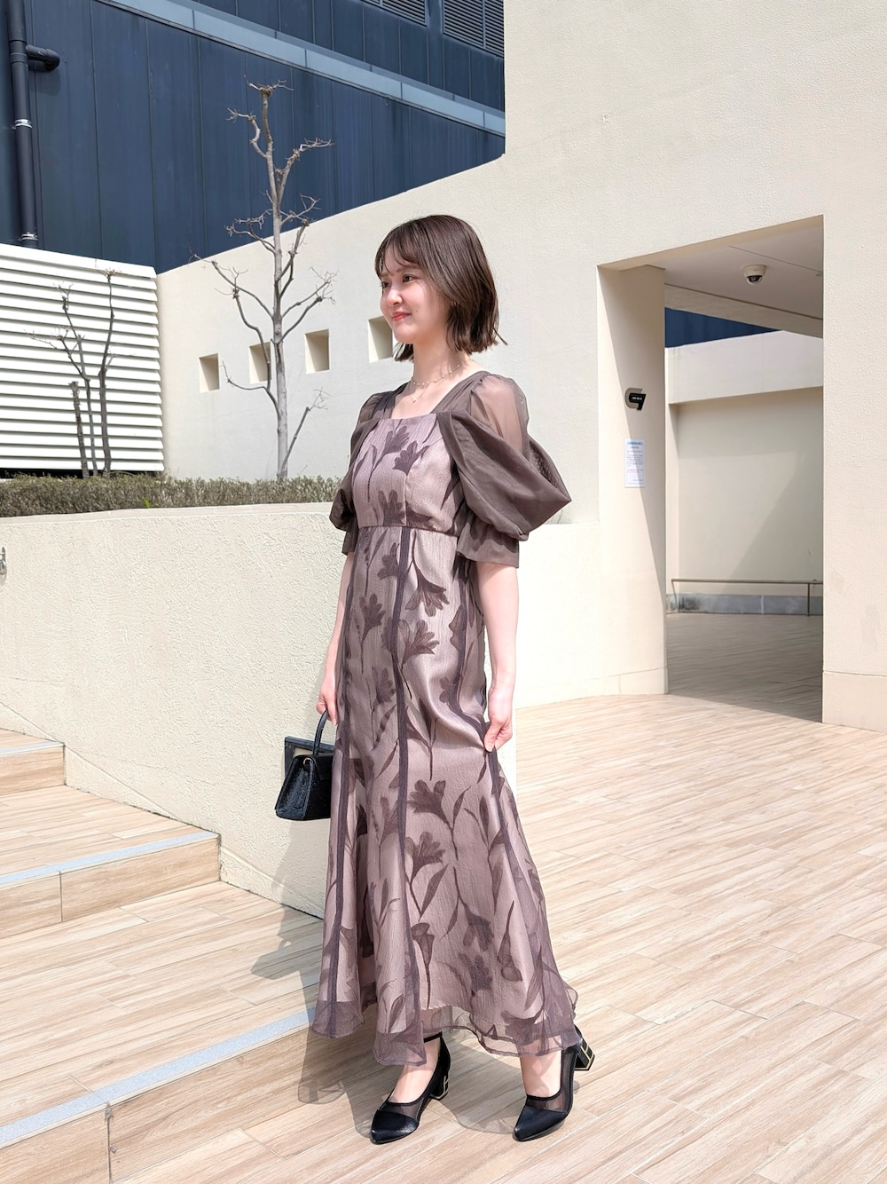 ブラウン系のドレス、ブラック系のパンプス、オレンジ系のワンピース/ドレスを着用したレディースの春コーディネートの1枚目の写真