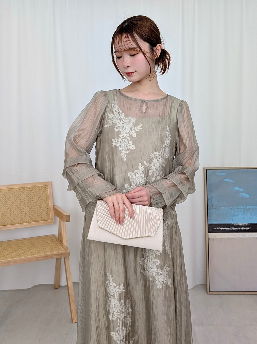 イエロー系のドレス、ベージュ系のクラッチバッグを着用したレディースの春コーディネートの1枚目の写真