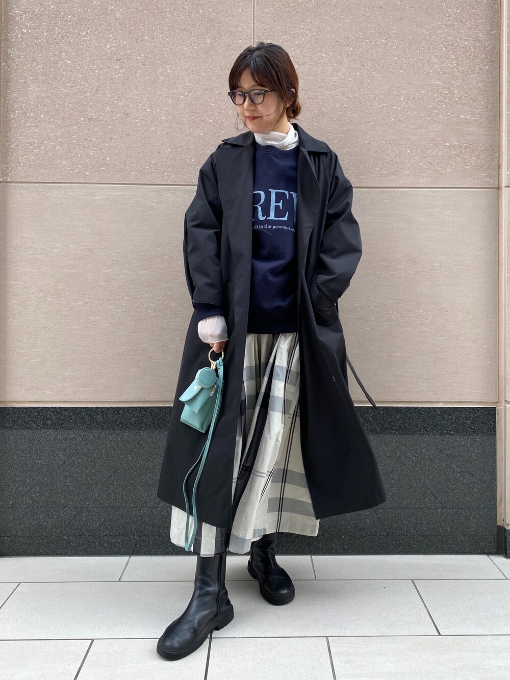ブラック系のステンカラーコート、ブルー系のスウェット、グリーン系のショルダーバッグを着用したレディースの冬コーディネートの2枚目の写真