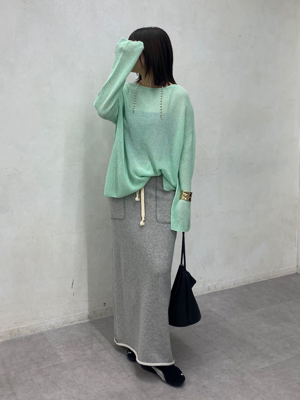 グリーン系のニット/セーター、グレー系のスカートを着用したレディースの春コーディネートの1枚目の写真
