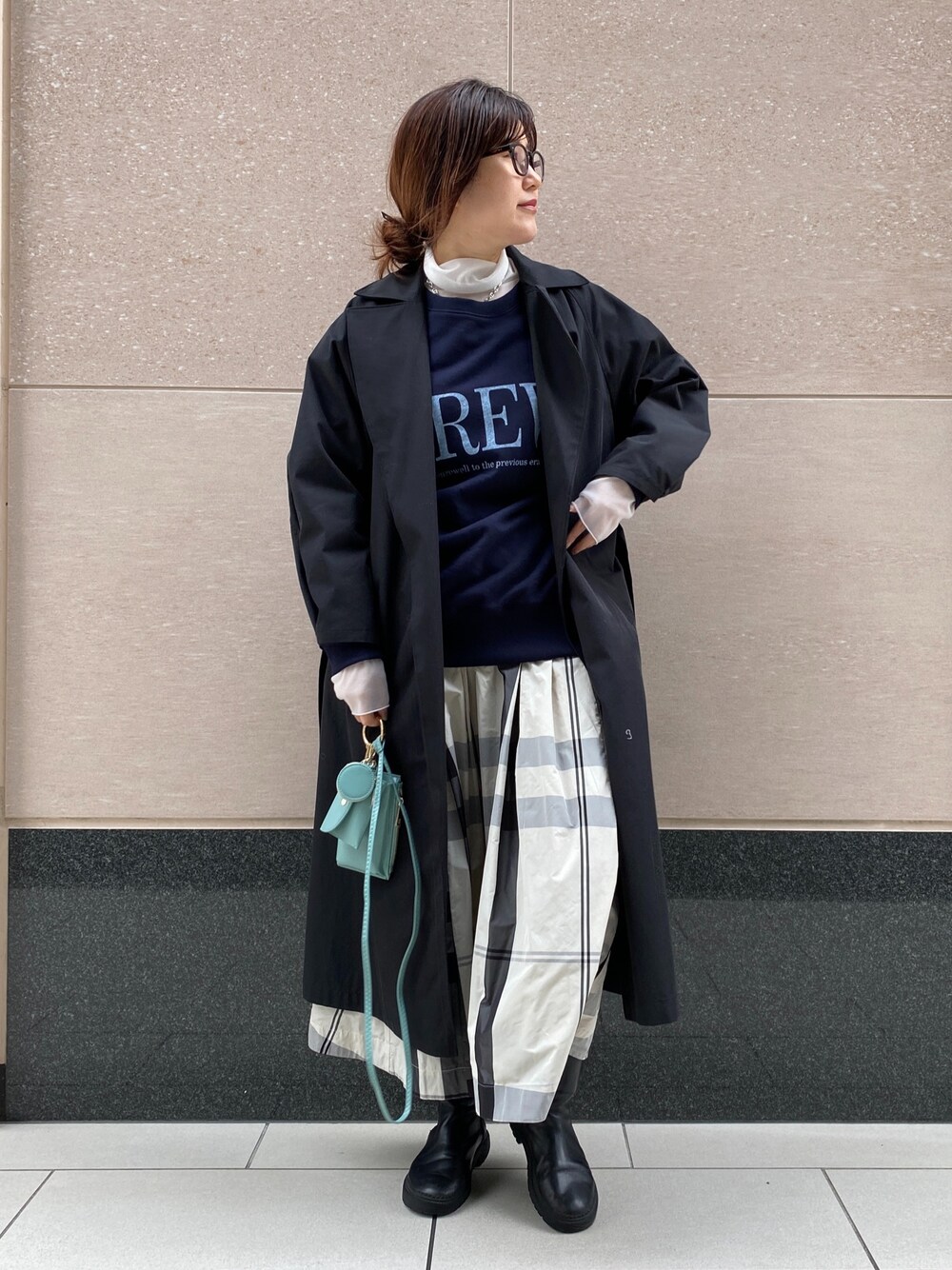 ブラック系のステンカラーコート、ブルー系のスウェット、グリーン系のショルダーバッグを着用したレディースの冬コーディネートの3枚目の写真