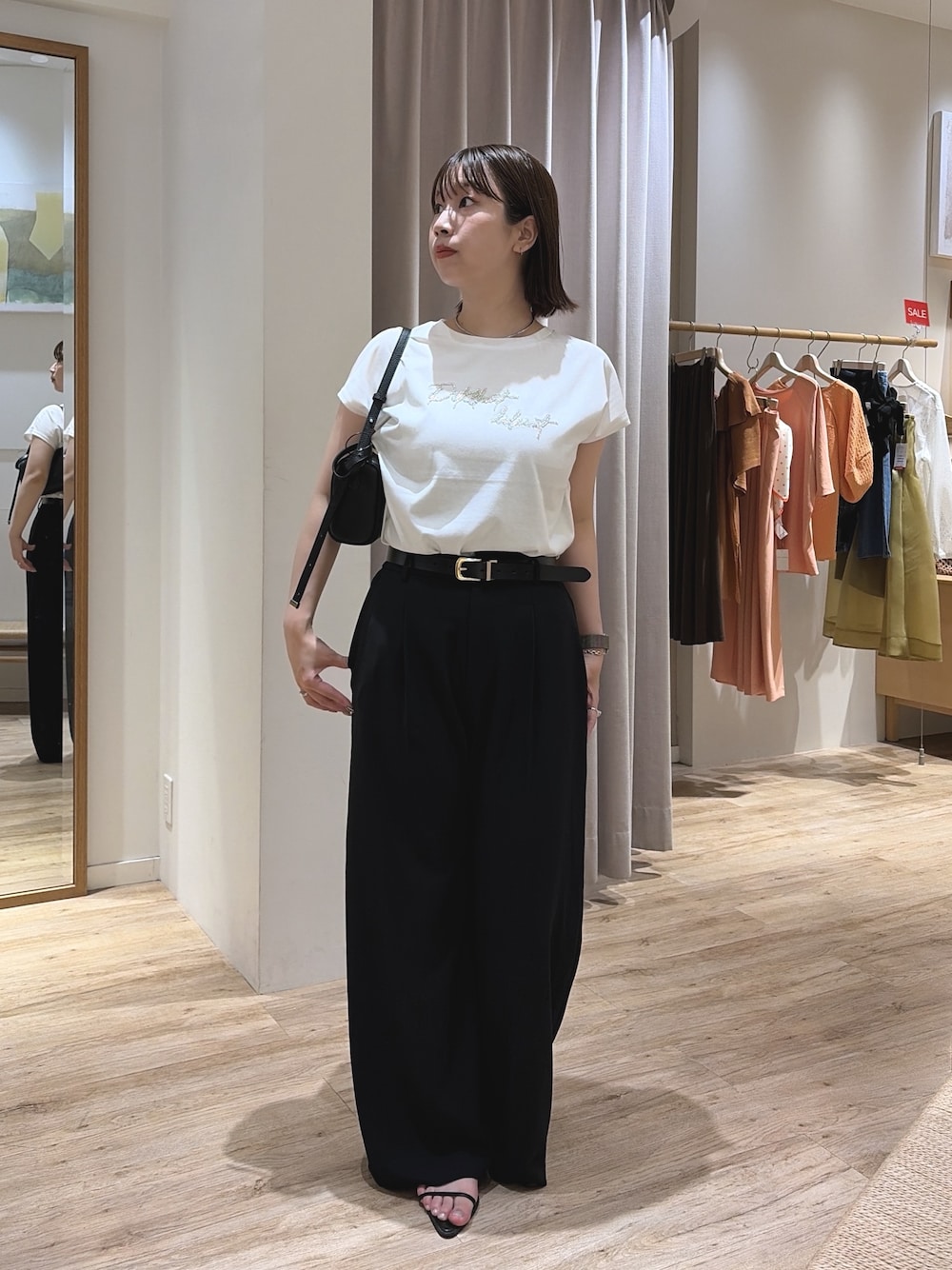 ブラック系のスラックス、ブラック系のショルダーバッグ、ホワイト系のTシャツ/カットソーを着用したレディースの夏コーディネートの1枚目の写真